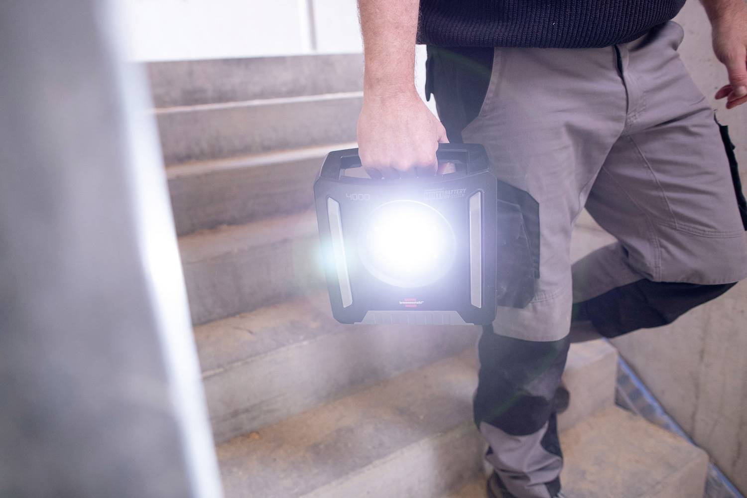 Une personne porte une lampe claire et brillante en montant les escaliers. La lampe éclaire le chemin, probablement pour assurer la sécurité ou pour des travaux de construction.