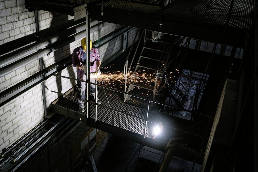 Une personne travaille avec un casque de protection et des lunettes de sécurité sur une rambarde dans un environnement industriel. Des étincelles jaillissent.