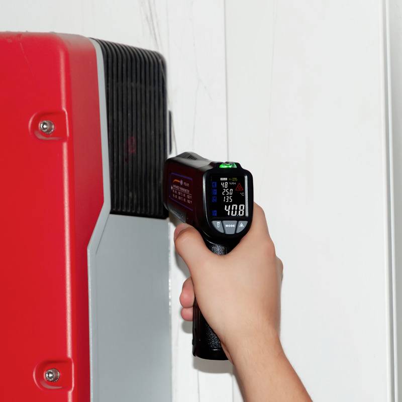 Une main tient un thermomètre infrarouge pointé vers une surface rouge. L'écran affiche une température de 40,8°C.