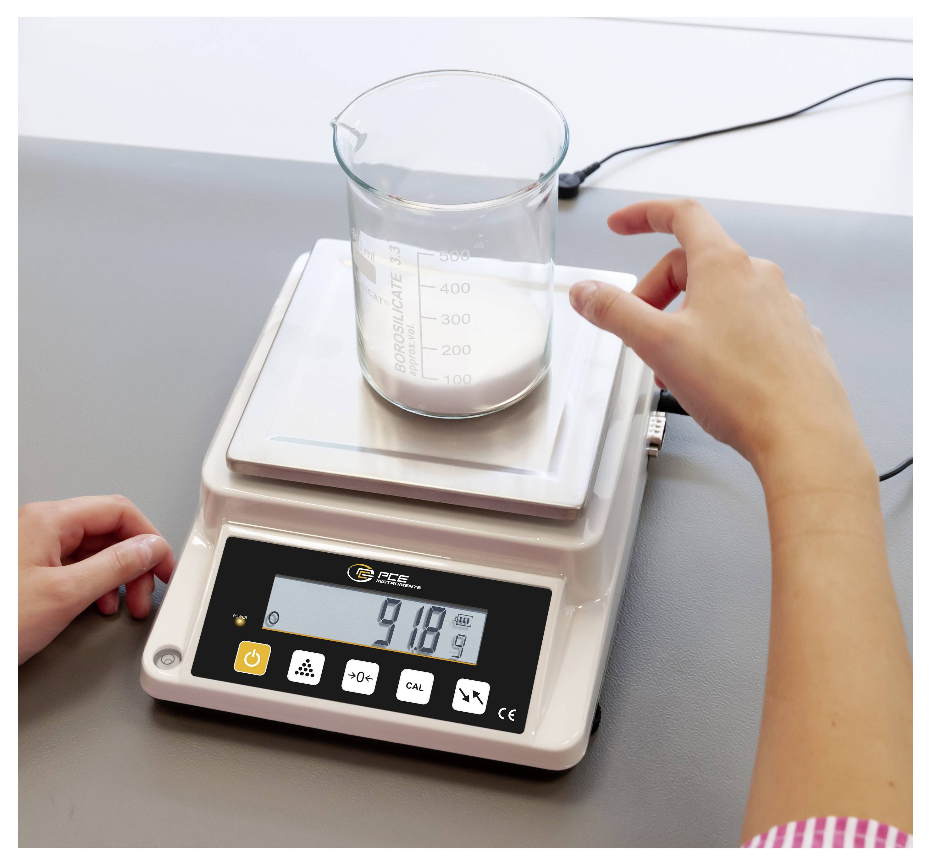 Une personne utilise une balance de laboratoire numérique pour peser un bécher contenant de la poudre blanche, l'affichage indiquant 91,8 g.