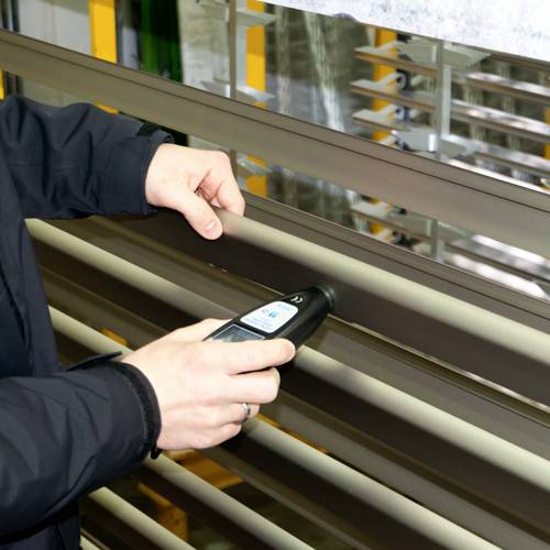 Une personne utilise un appareil portable pour mesurer ou ajuster des stores. La scène est centrée sur l'utilisation et la fonctionnalité.