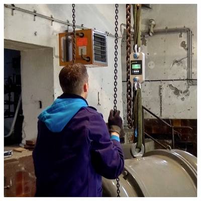 Un ouvrier actionne un palan à chaîne suspendu à côté d'un grand réservoir cylindrique dans un atelier industriel.