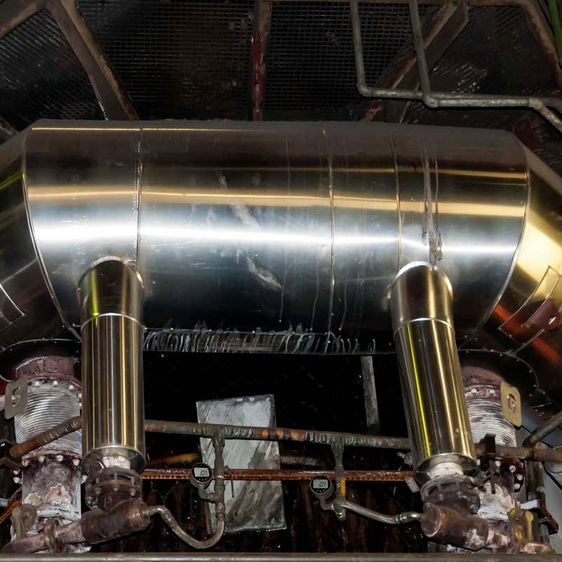 Un grand cylindre métallique industriel avec deux tubes saillants est monté de manière centrale, entouré de tuyauteries et de vannes.