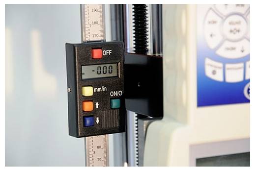 Jauge de mesure numérique sur une échelle verticale avec un affichage indiquant 0,00 et des commandes mm/po, montée sur une machine d'essai.