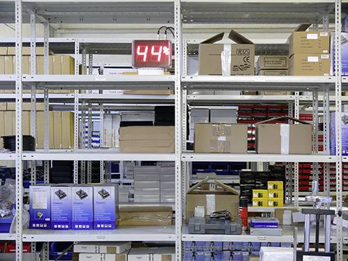 Étagère de rangement avec des cartons, des colis et un affichage électronique indiquant '44%' en haut à gauche.