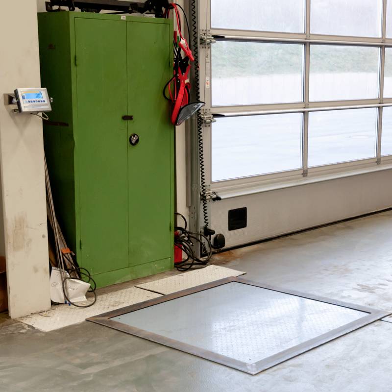 Espace baigné de lumière avec une armoire verte, une balance au sol et un écran de contrôle au mur ; équipements pour la mesure du poids.