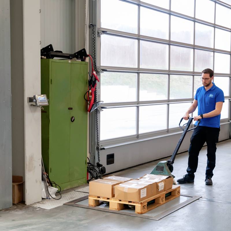 Un employé transporte une palette à l'aide d'un chariot élévateur dans un entrepôt doté de grandes fenêtres.