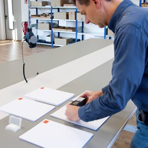Une personne numérise des feuilles blanches avec un scanner portable dans un bureau avec des étagères en arrière-plan.
