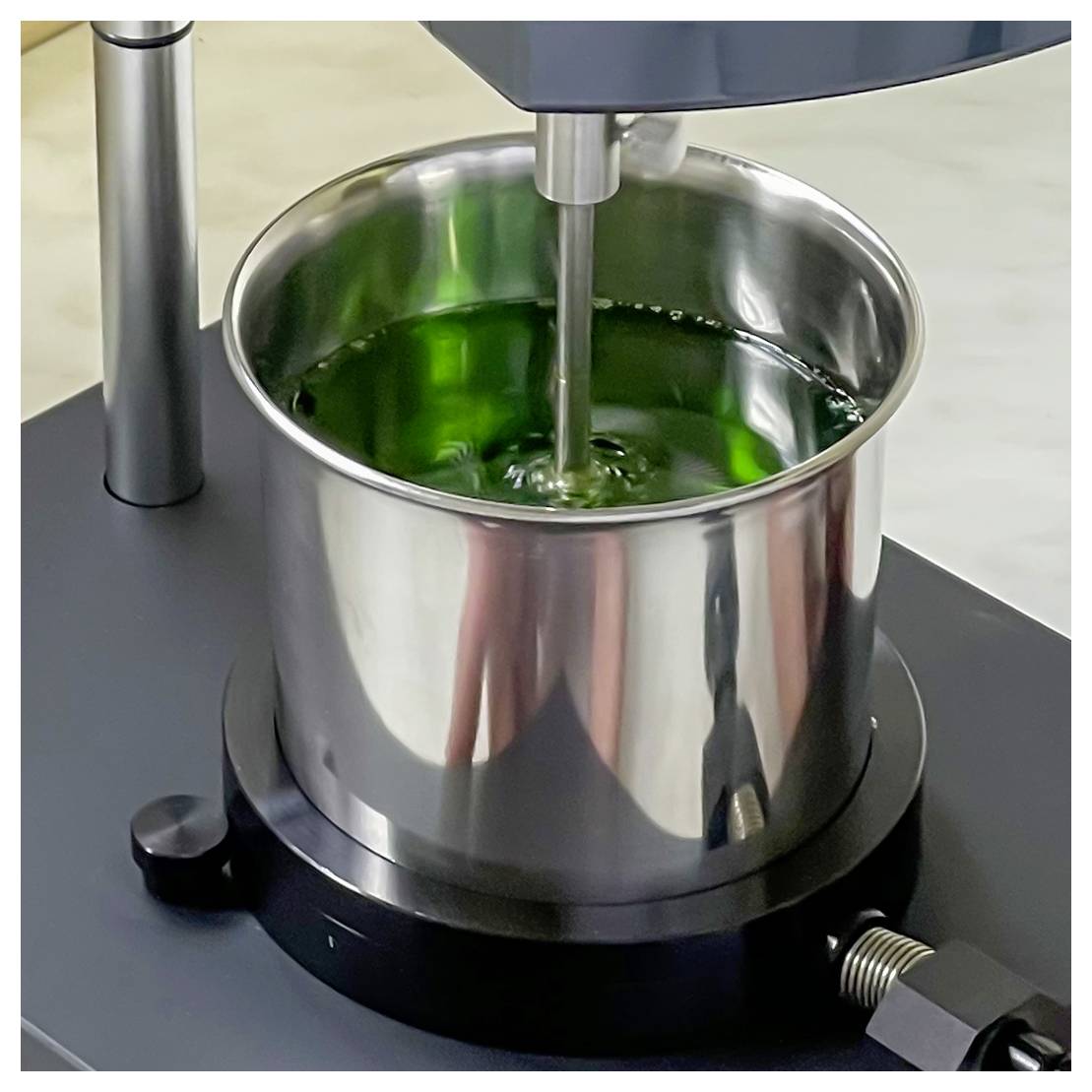 Un récipient de mélange en métal contient un liquide vert tandis qu'un arbre central le mélange sur une machine à mélanger de laboratoire ou industrielle.