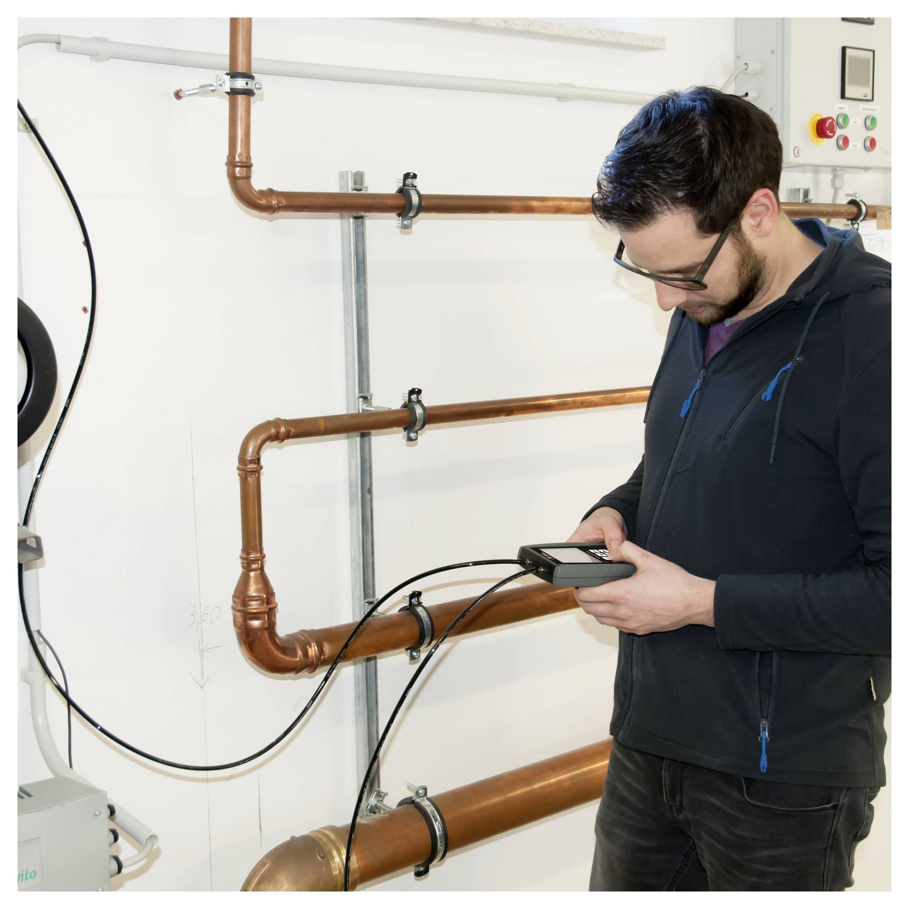 Technicien inspectant des tuyaux en cuivre avec un appareil portatif dans une chaufferie.