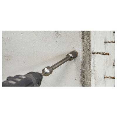 Une perceuse avec un foret à maçonnerie perce un trou dans un mur en béton près d'une armature métallique exposée.