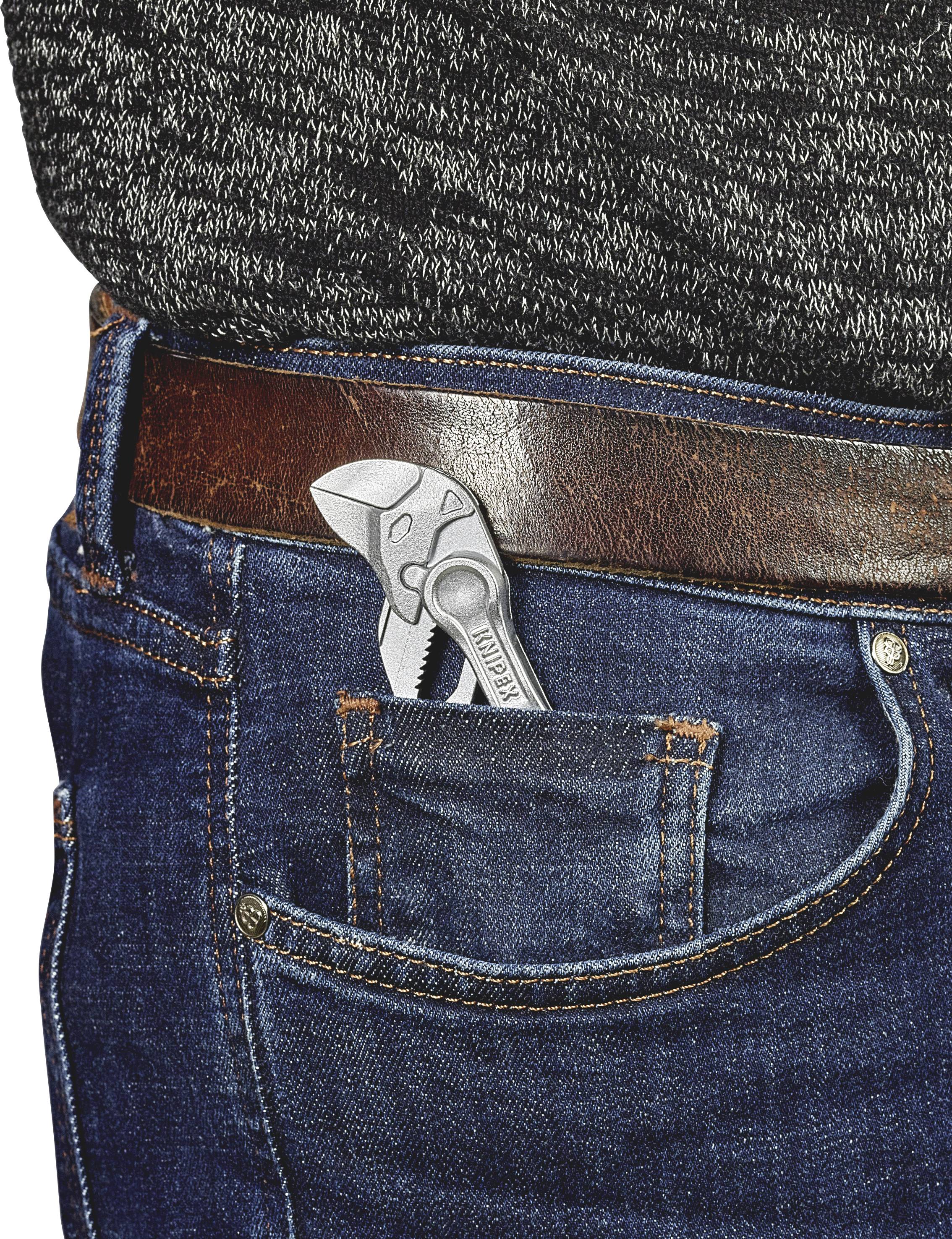 Une petite pince métallique est coincée dans la poche arrière d'un jean bleu, maintenu par une ceinture en cuir marron.