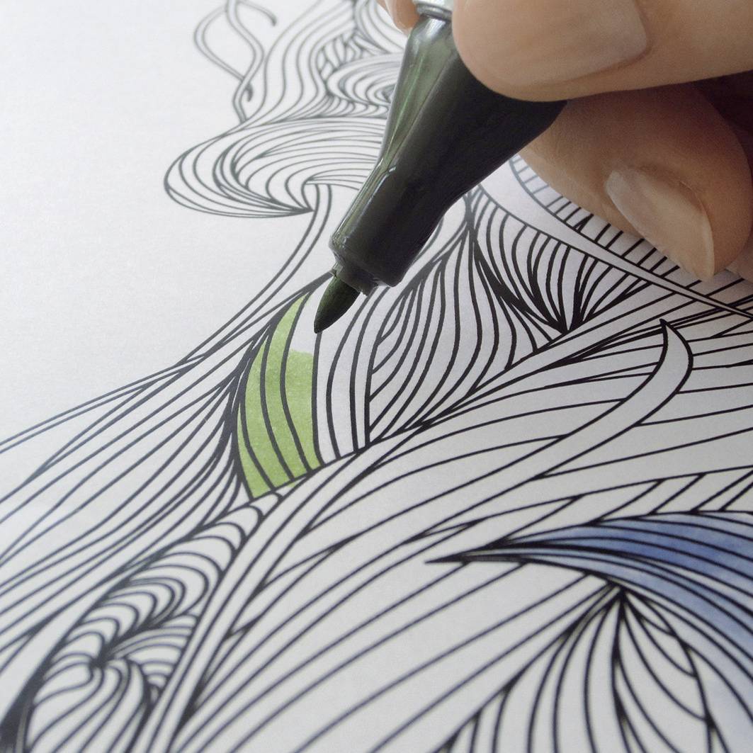 Une main tient un stylo et colorie un motif de feuille verte dans un dessin détaillé à colorier.