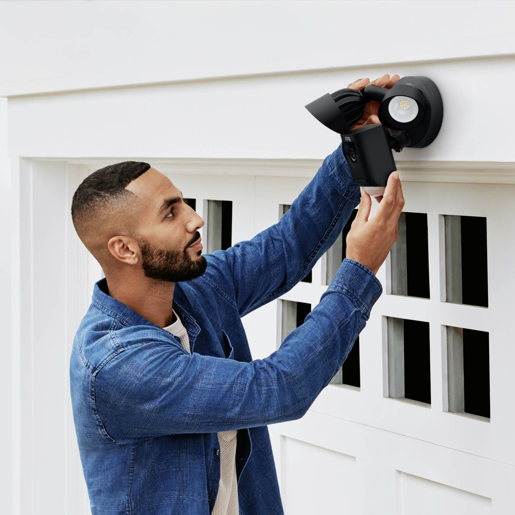 Un homme installe une caméra de sécurité sur le mur extérieur d'un bâtiment. La caméra est grande et noire, prête à surveiller.