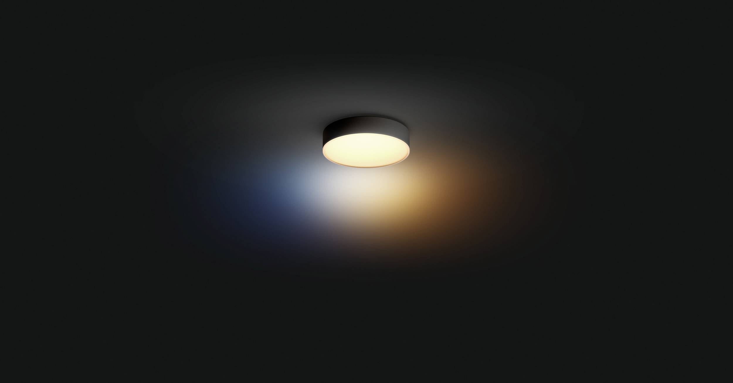 Un luminaire circulaire au plafond diffuse une lumière blanche et légèrement colorée sur un plafond sombre, s'estompant progressivement vers l'extérieur.