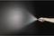 Une main tient une lampe de poche et projette de la lumière sur une surface sombre.