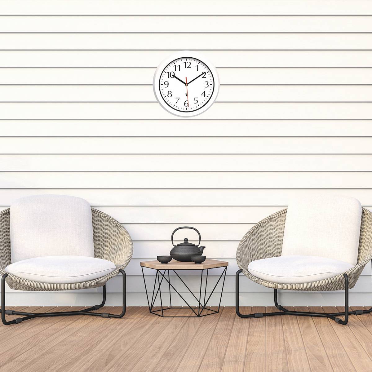 Deux fauteuils en rotin avec des coussins blancs sont disposés autour d'une petite table sur laquelle repose une théière. Une horloge indique 10h10 sur le mur.