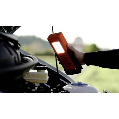 Une personne vérifie le moteur d'une voiture à l'extérieur avec une lampe portable lumineuse afin d'améliorer sa visibilité.