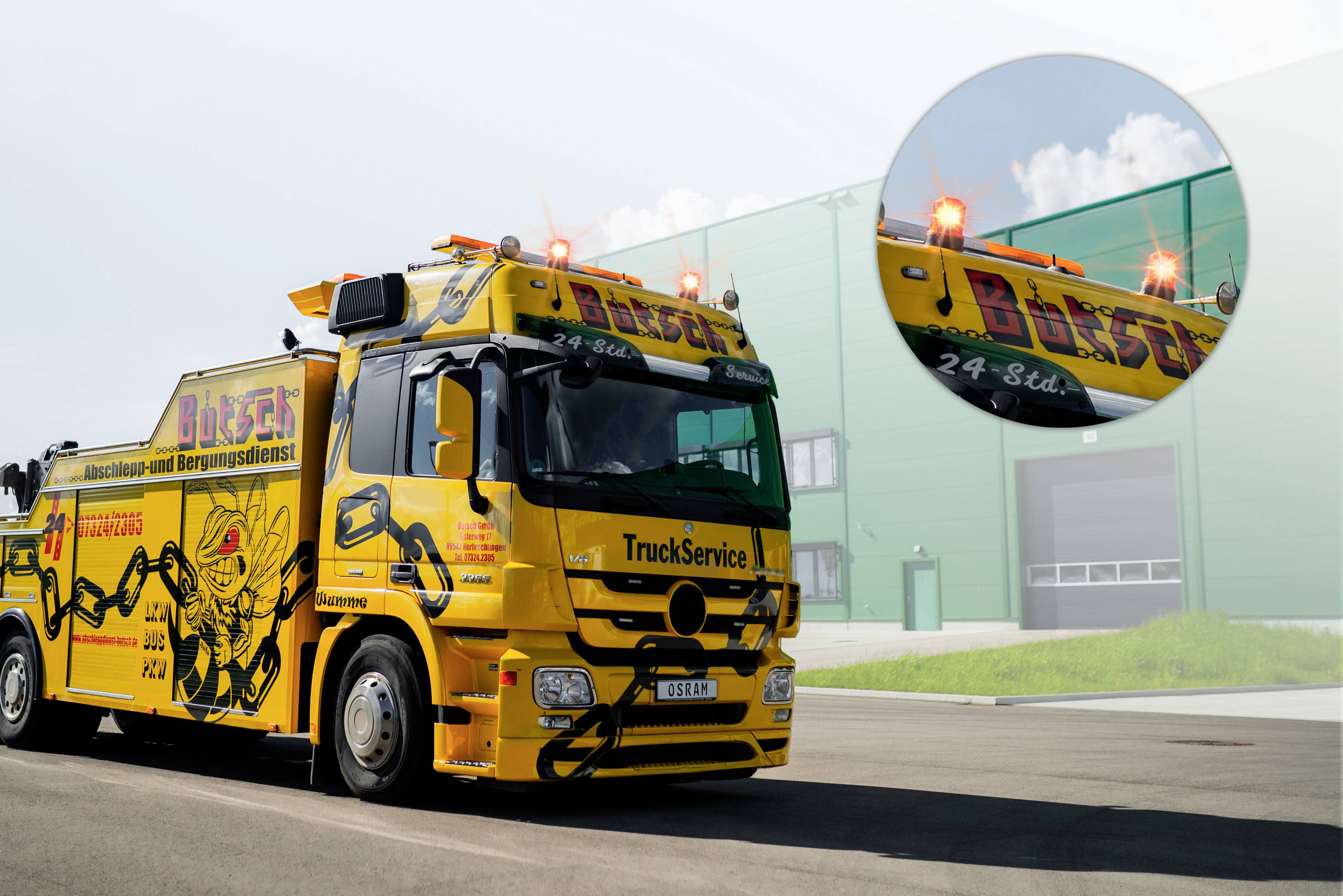 Camion de dépannage jaune avec des gyrophares et l'inscription 'Bösch' sur le côté, stationné devant un grand bâtiment vert.