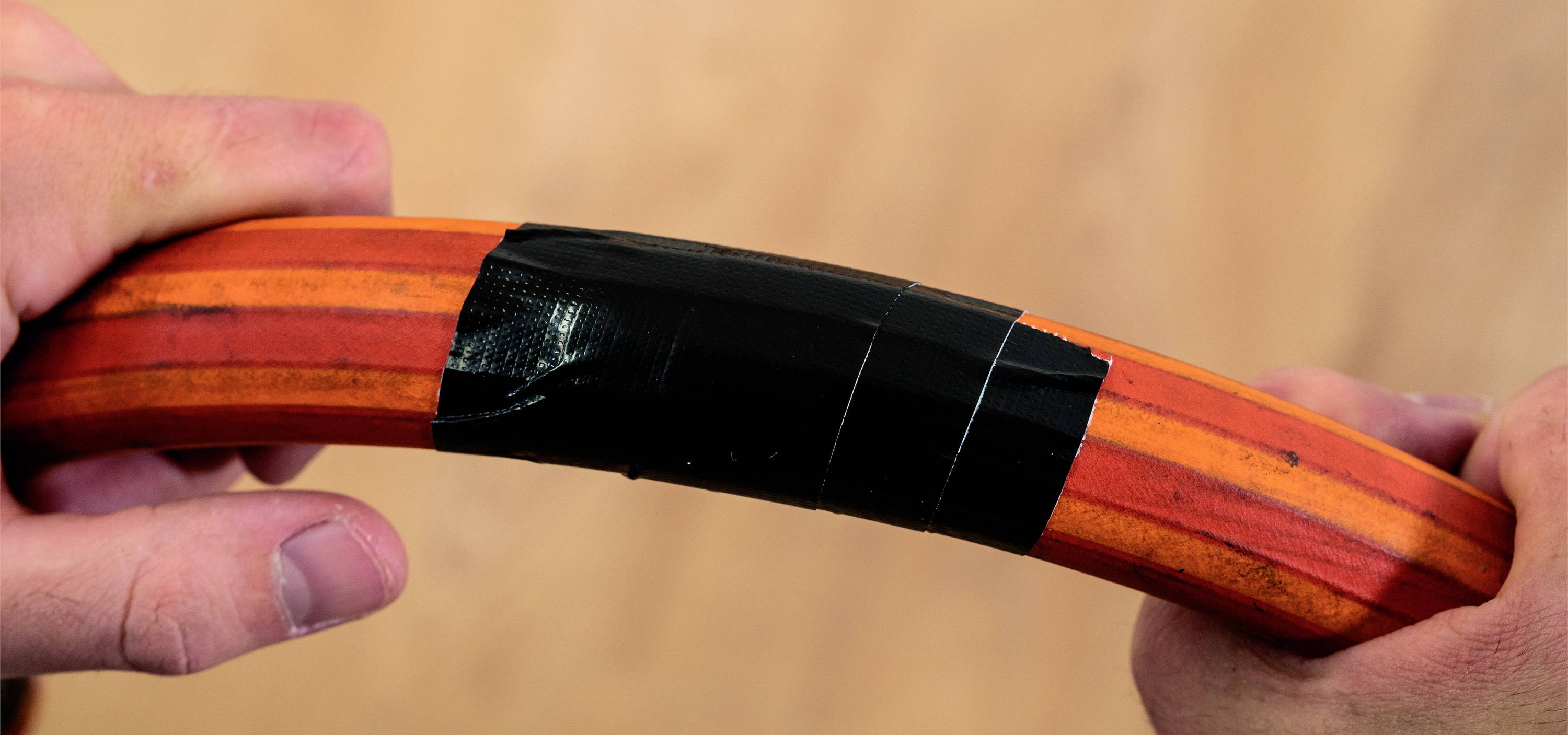 Deux mains tiennent un tuyau courbé orange avec des rayures rouges, enroulé de ruban adhésif noir.