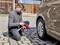 Une personne est agenouillée sur un pavé et utilise un dispositif portable pour vérifier la pression des pneus d'une voiture.