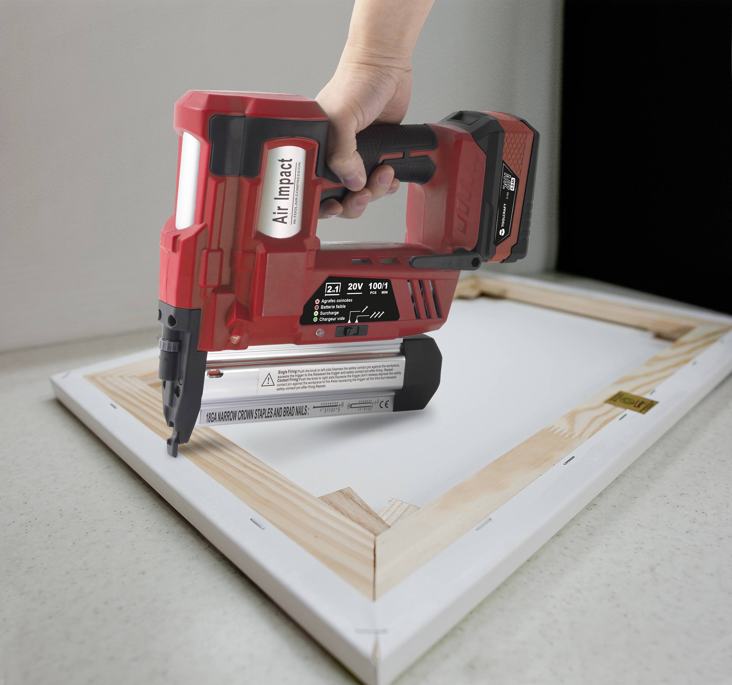 Une main tient un cloueur à batterie rouge et fixe une toile sur un cadre en bois. L'appareil est étiqueté 'Air Impact'.