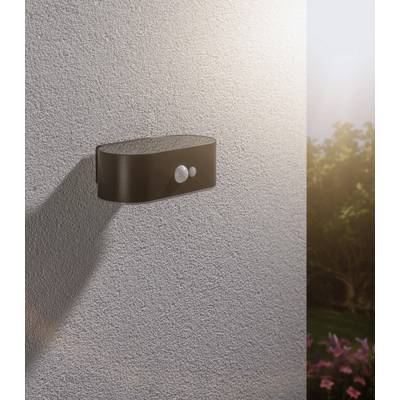 Lampe extérieure avec détecteur de mouvement sur un mur de maison, ciel ensoleillé en arrière-plan, éclairant la zone de jardin dans l'obscurité.