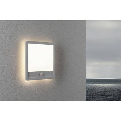 Lampe extérieure illuminant un mur avec vue sur la mer. Le ciel est nuageux. La lampe arbore un design simple et moderne.