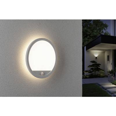 Une lampe extérieure ronde moderne avec détecteur de mouvement est fixée sur un mur de maison. En arrière-plan, on aperçoit une entrée avec un chemin éclairé.