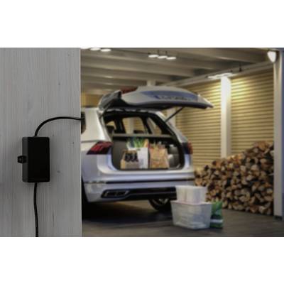 Une voiture garée dans un carport avec le hayon ouvert. Des sacs de courses sont dans le coffre. Au premier plan, un chargeur est fixé au mur.