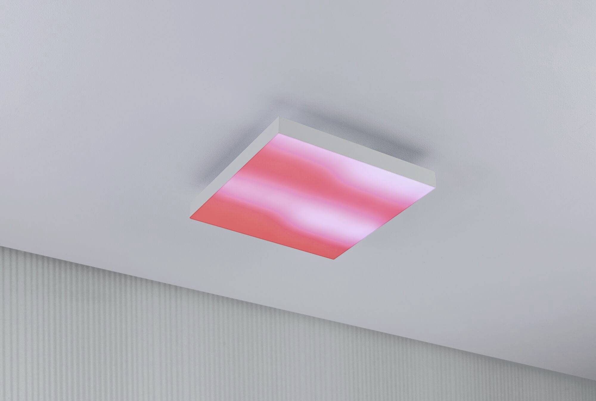 Un luminaire de plafond LED rectangulaire rose éclaire une pièce simple et moderne.