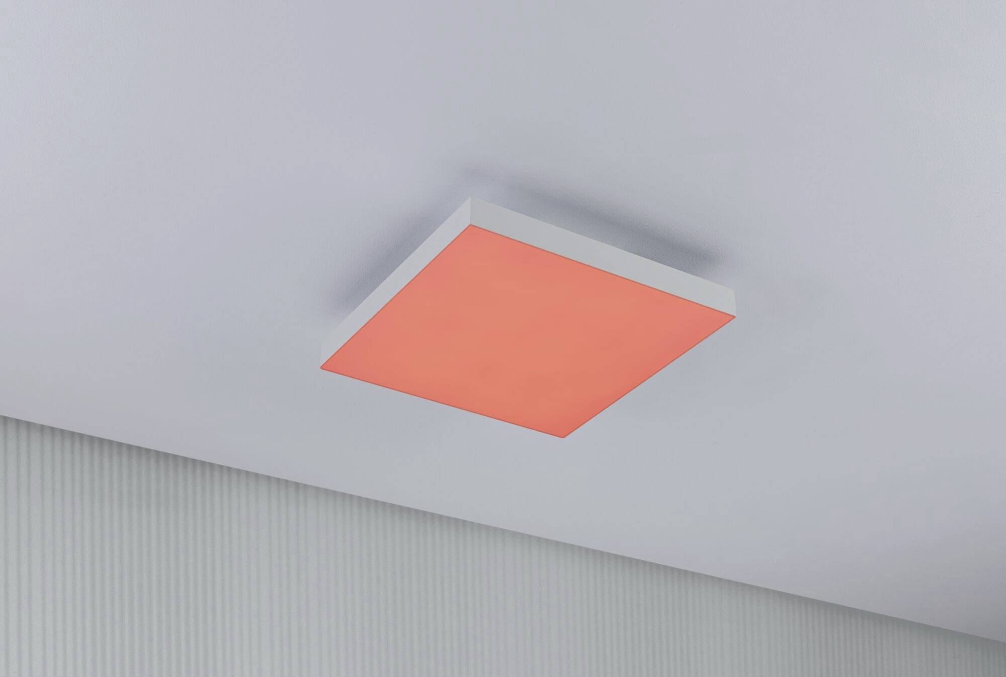 Un luminaire carré avec lumière rouge, installé sur un plafond blanc, est suspendu au-dessus d'un mur gris clair.