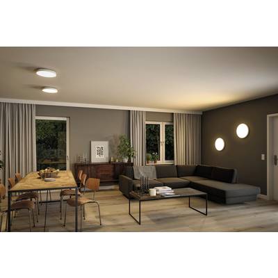 Salon confortable avec table à manger, chaises, canapé gris foncé, table basse et lampes fixées au mur et au plafond, des arbres visibles à l'extérieur.