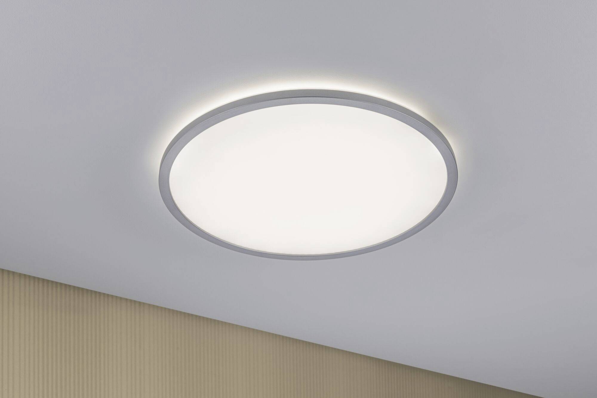 Un luminaire circulaire de plafond émettant une lumière blanche est installé au plafond d'une pièce. En dessous se trouve un mur beige.