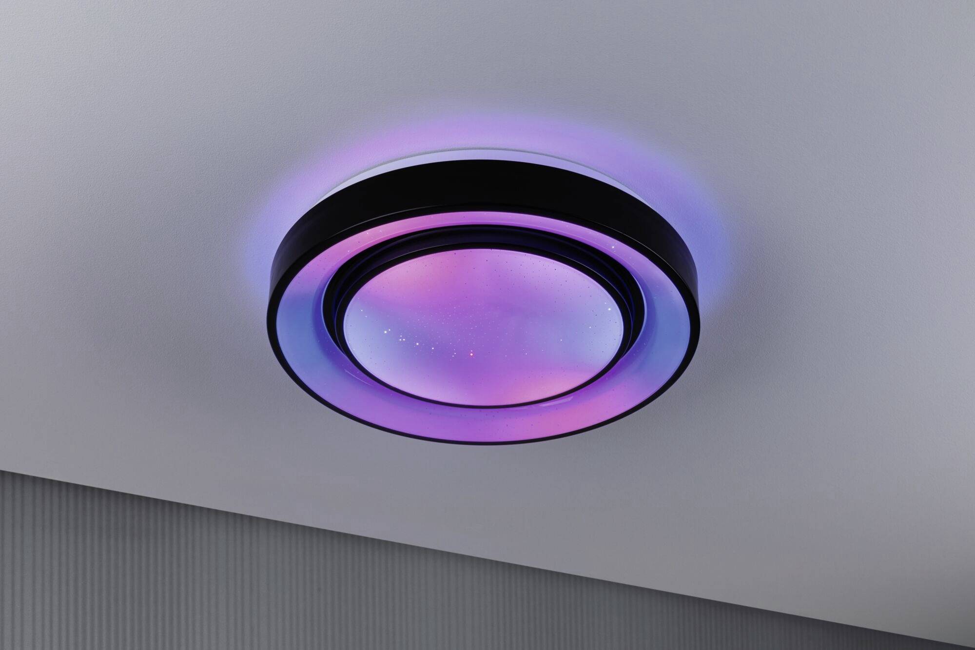Plafonnier LED à changement de couleur sur un plafond blanc, avec des reflets violets et bleus. Design moderne à forme circulaire.