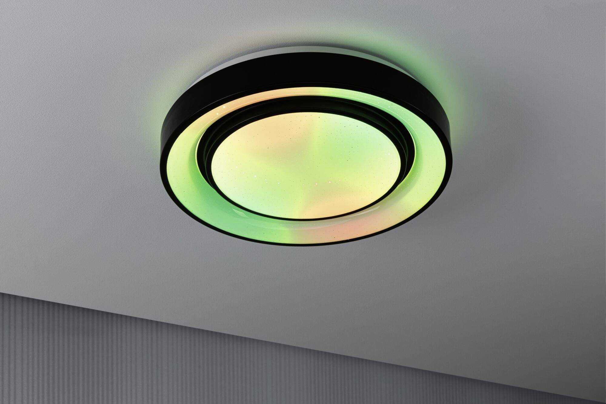 Plafonnier rond avec éclairage LED multicolore, principalement vert et orange, monté sur un plafond blanc.