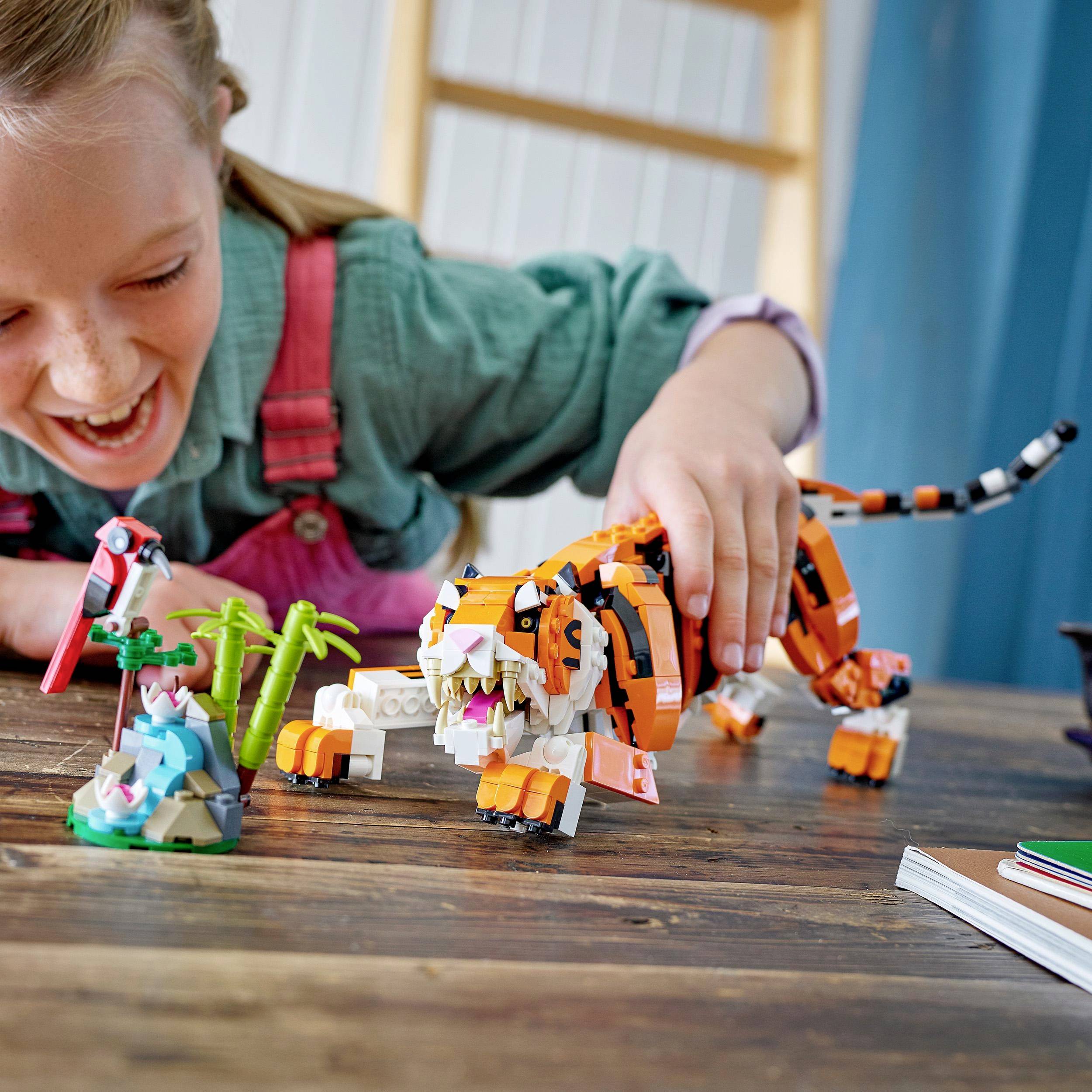 Un enfant joue en souriant avec un jouet de tigre coloré en blocs de construction et un paysage de palmiers sur une table.