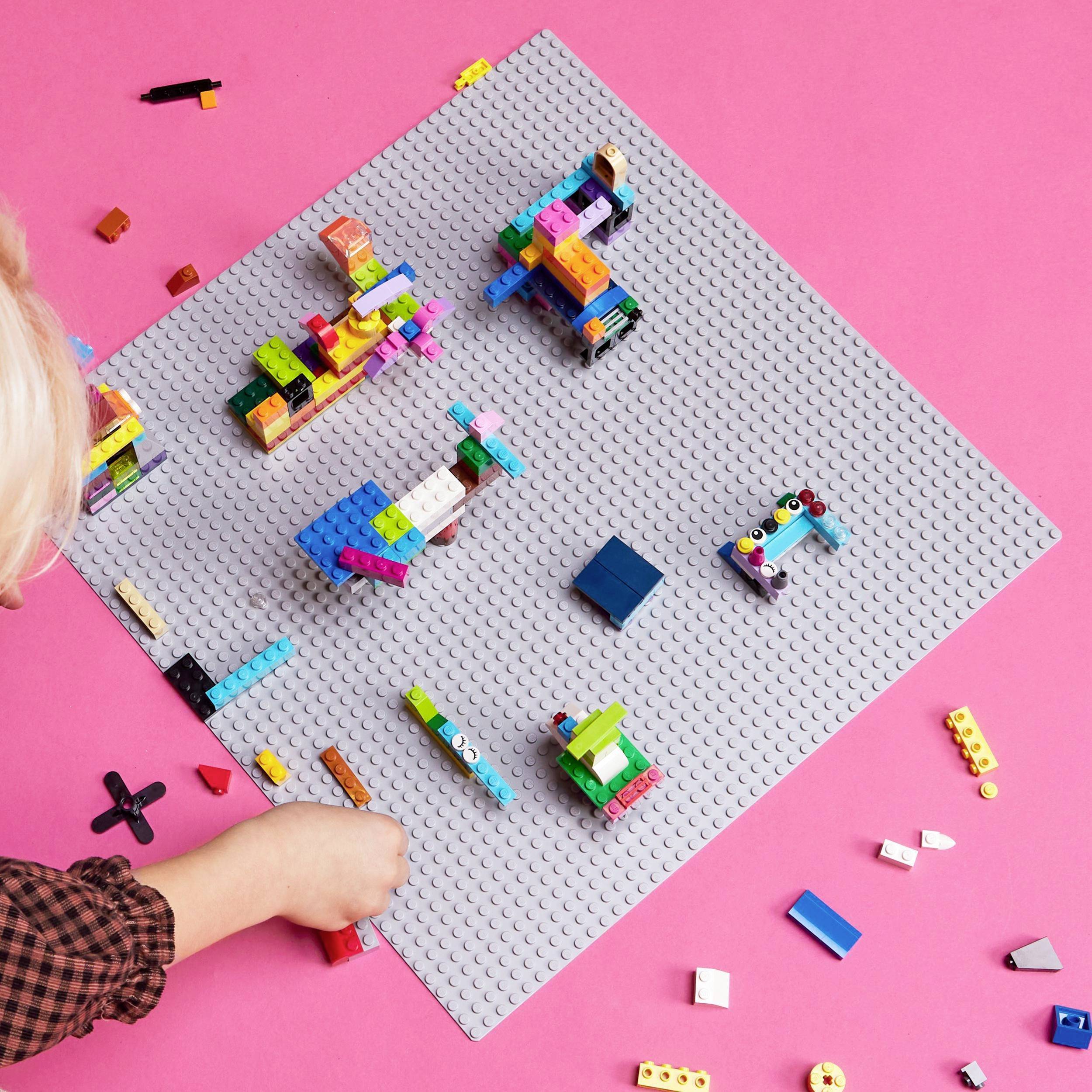Un enfant joue avec des blocs de construction colorés sur une grande plaque de construction grise, posée sur un support rose.