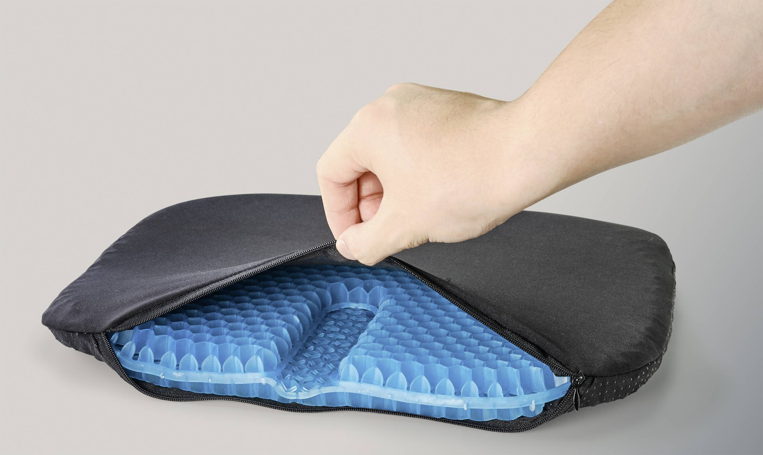 Une main soulève un tissu noir, révélant un coussin de gel bleu et texturé en dessous.