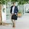Un homme vêtu d'un costume d'affaires marche en souriant dans un immeuble de bureaux moderne. Il porte un sac pour ordinateur portable noir dans sa main droite.