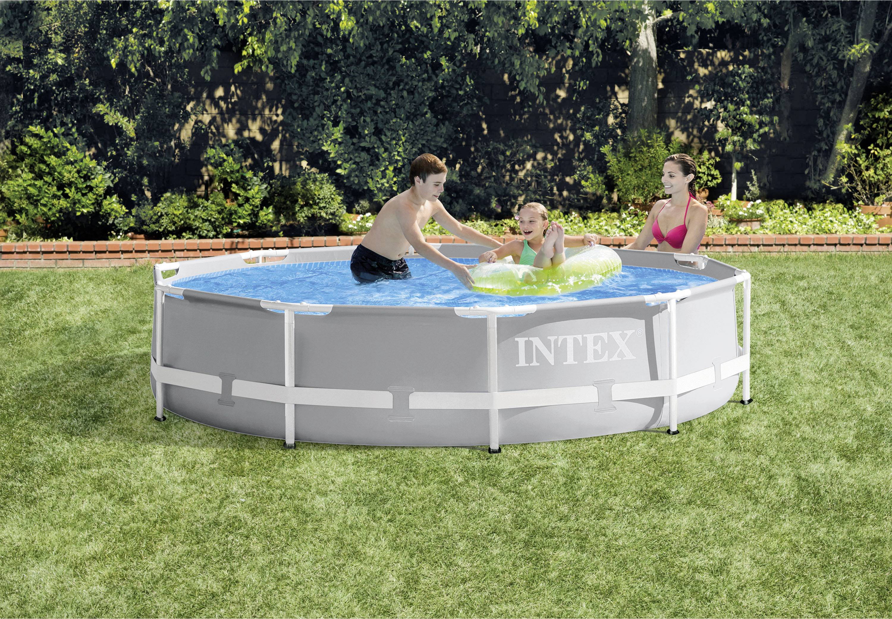 Trois personnes jouent dans une piscine ronde hors-sol dans un jardin. Une personne plonge, tandis que les autres sont assises au bord du bassin et regardent.
