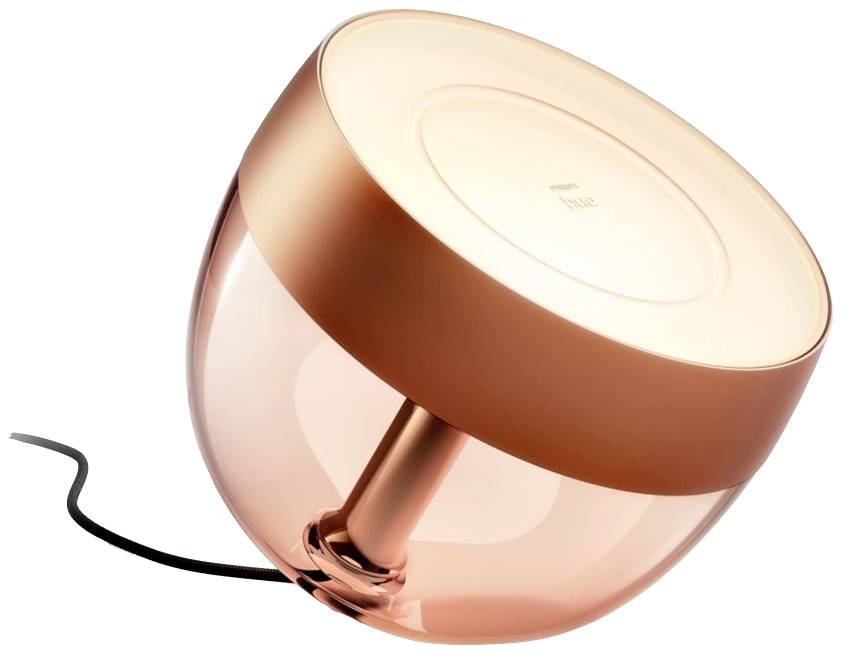 Lampe de table moderne en or rose, de forme ronde et dotée d'un socle transparent. Elle est légèrement inclinée et possède un câble électrique noir.