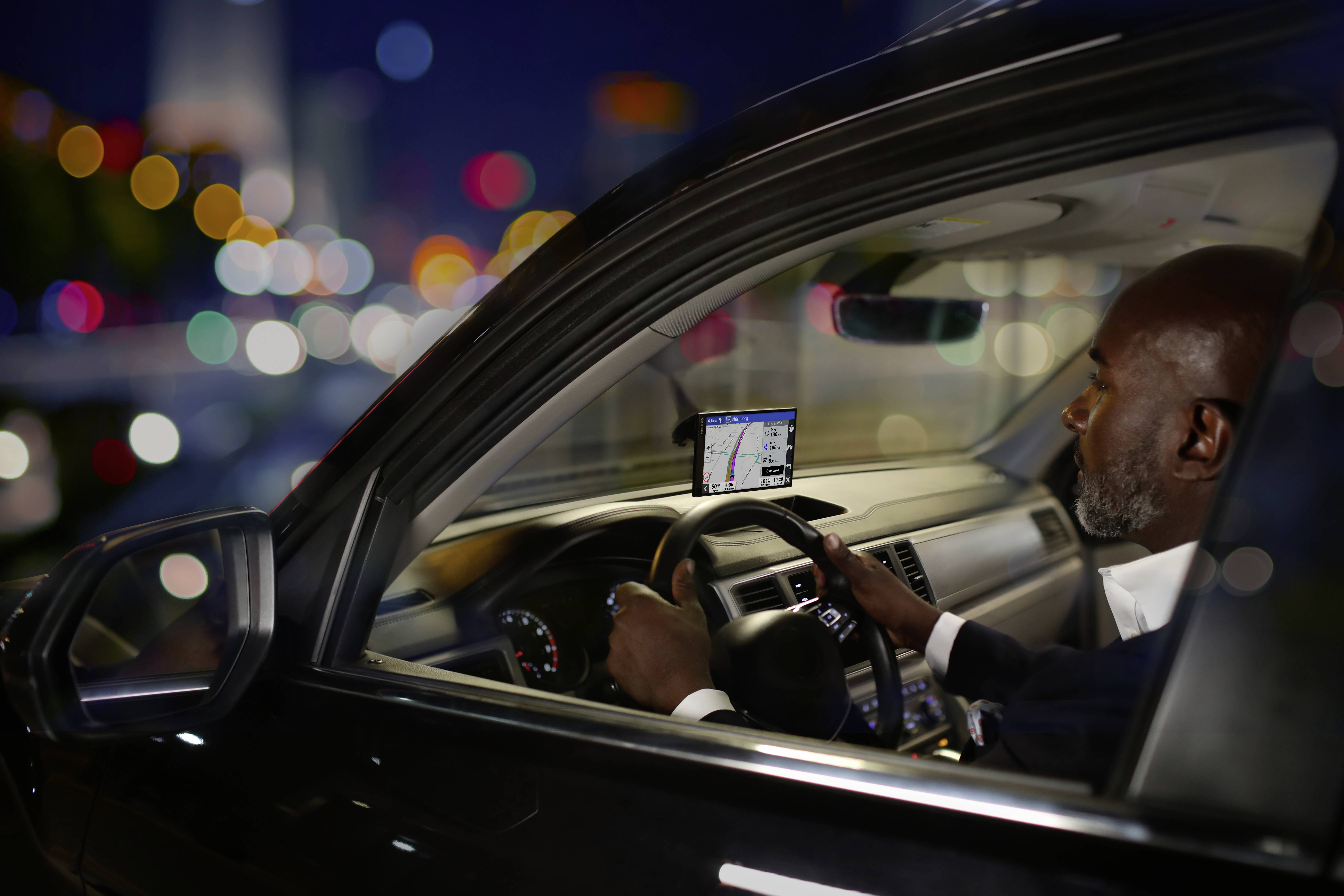Un homme conduit une voiture à travers une ville illuminée la nuit, en utilisant un système de navigation.