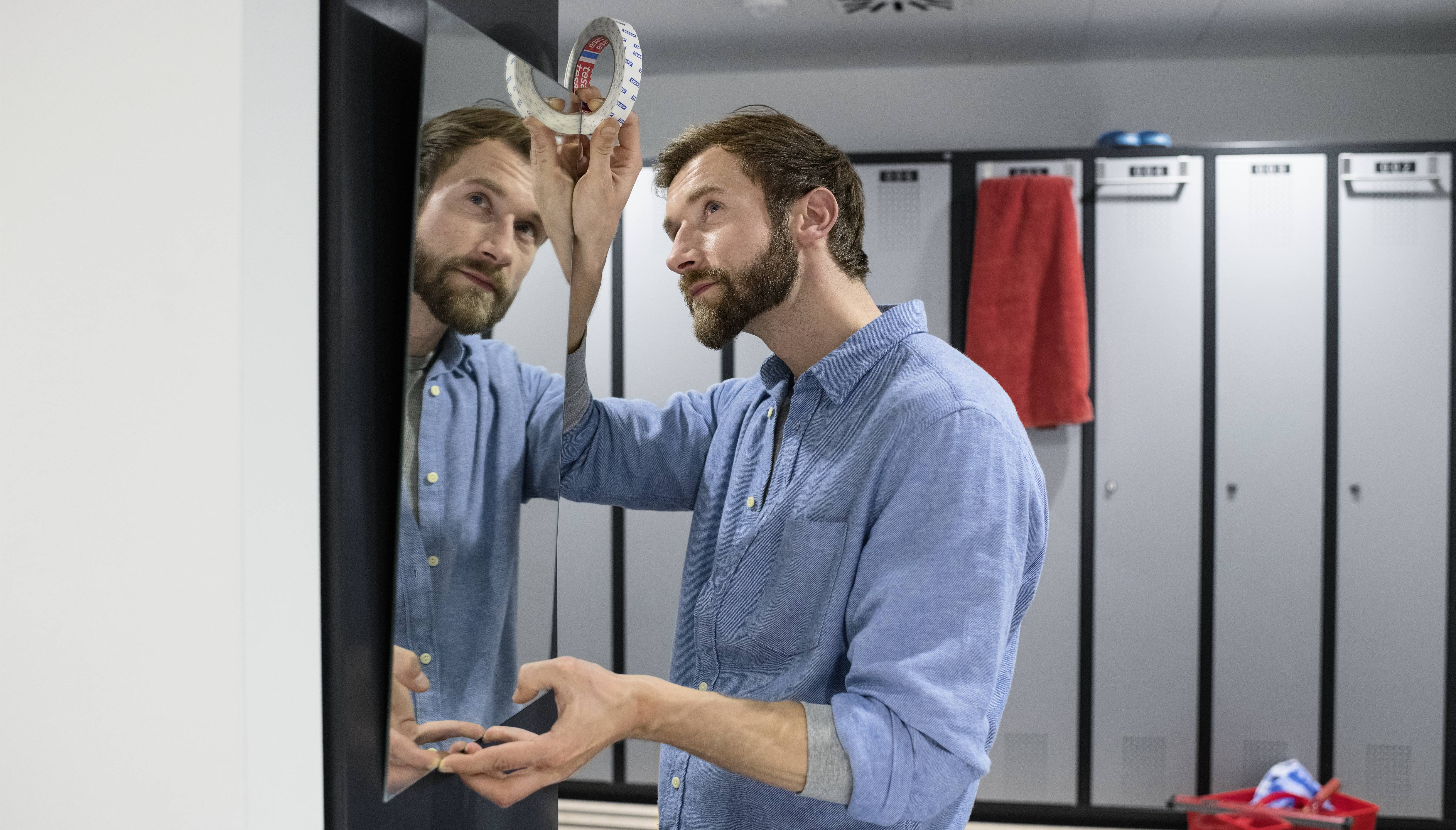 Un homme en chemise bleue regarde avec admiration un trophée en brique dans le miroir d'un vestiaire avec des casiers.