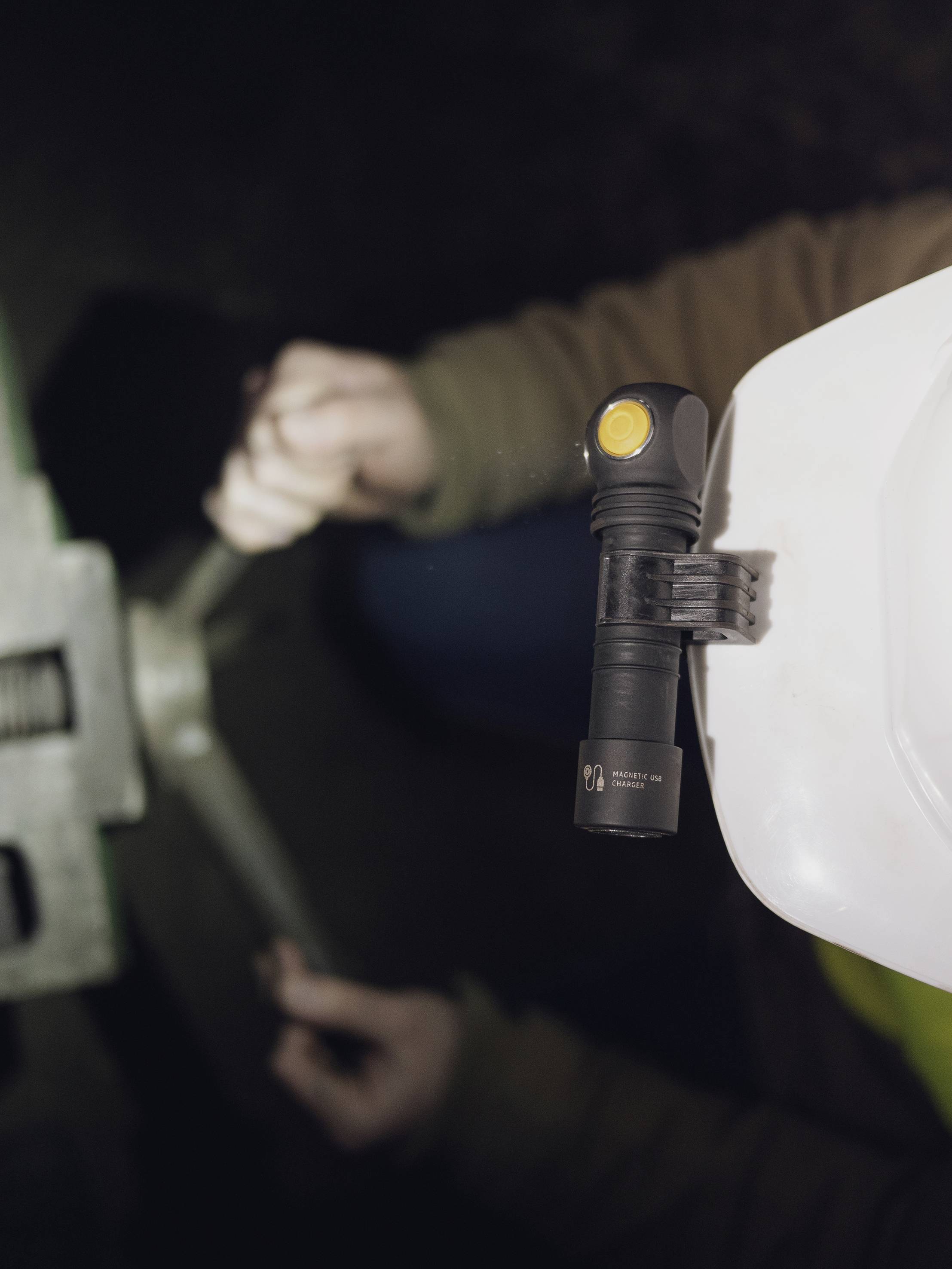 Une personne porte un casque de protection blanc avec une lampe frontale et travaille avec une clé à molette sur une machine.