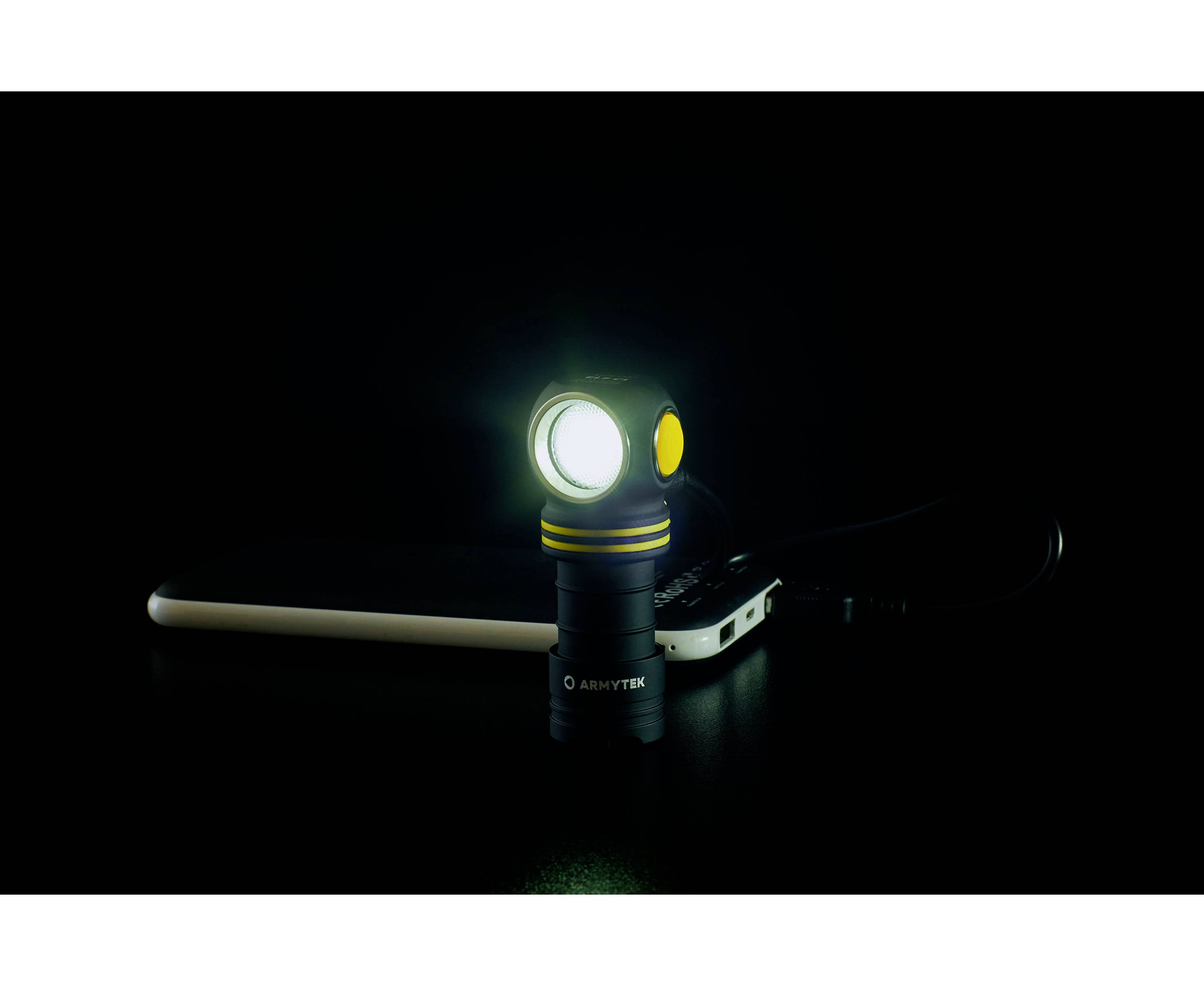 Une petite lampe de poche brille sur un fond sombre, posée à côté d'un smartphone.
