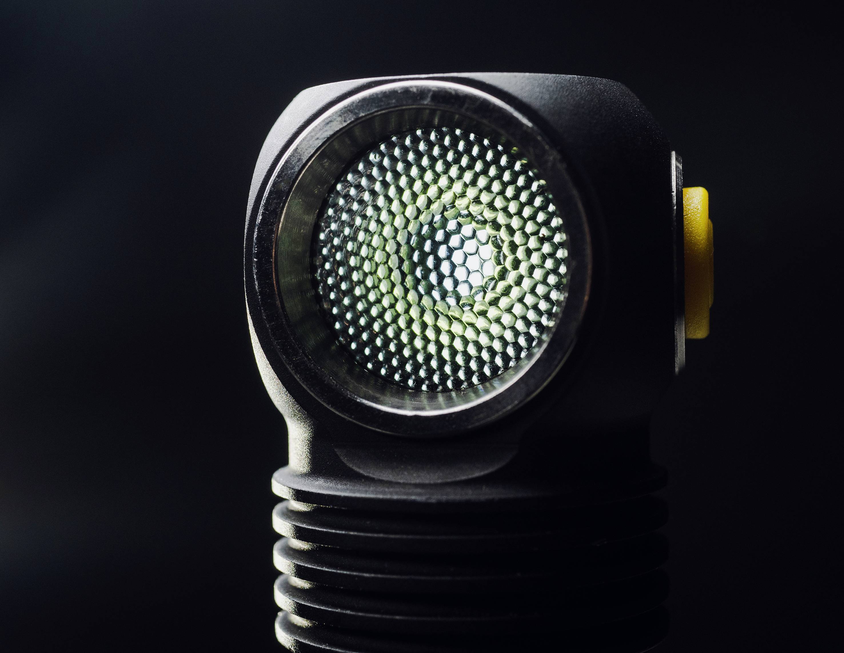 Un gros plan d'une lampe de poche avec un motif hexagonal sur le verre. La lumière est allumée, encadrée par un arrière-plan sombre.