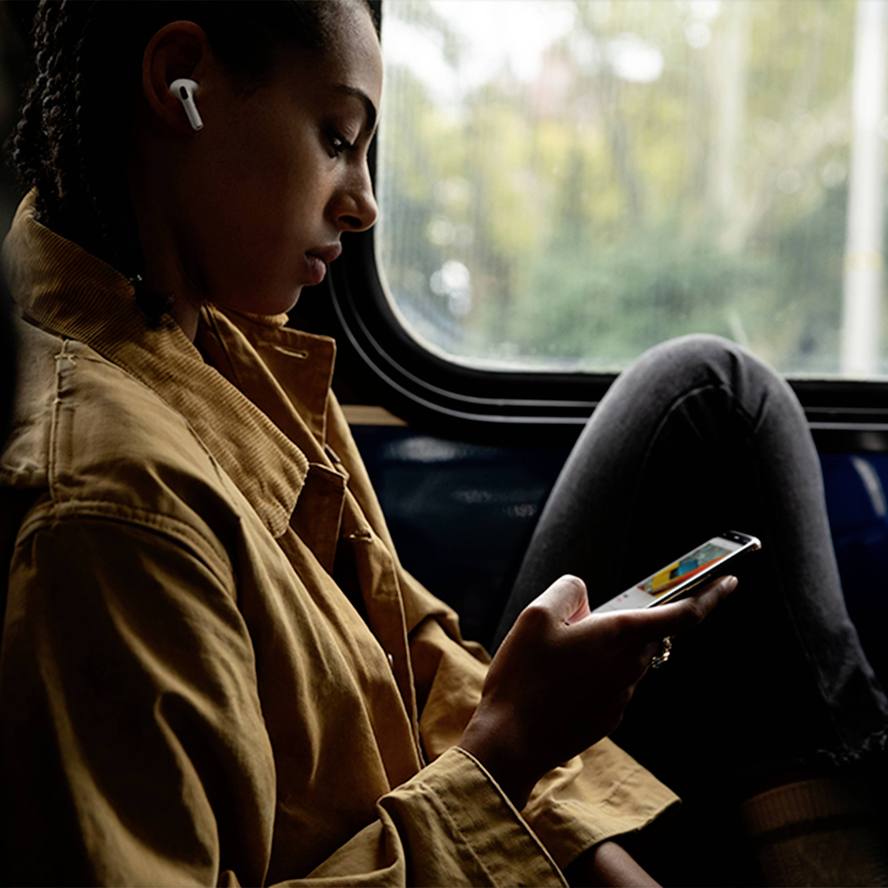 Une personne est assise dans un train, porte des écouteurs sans fil et regarde quelque chose sur son smartphone.