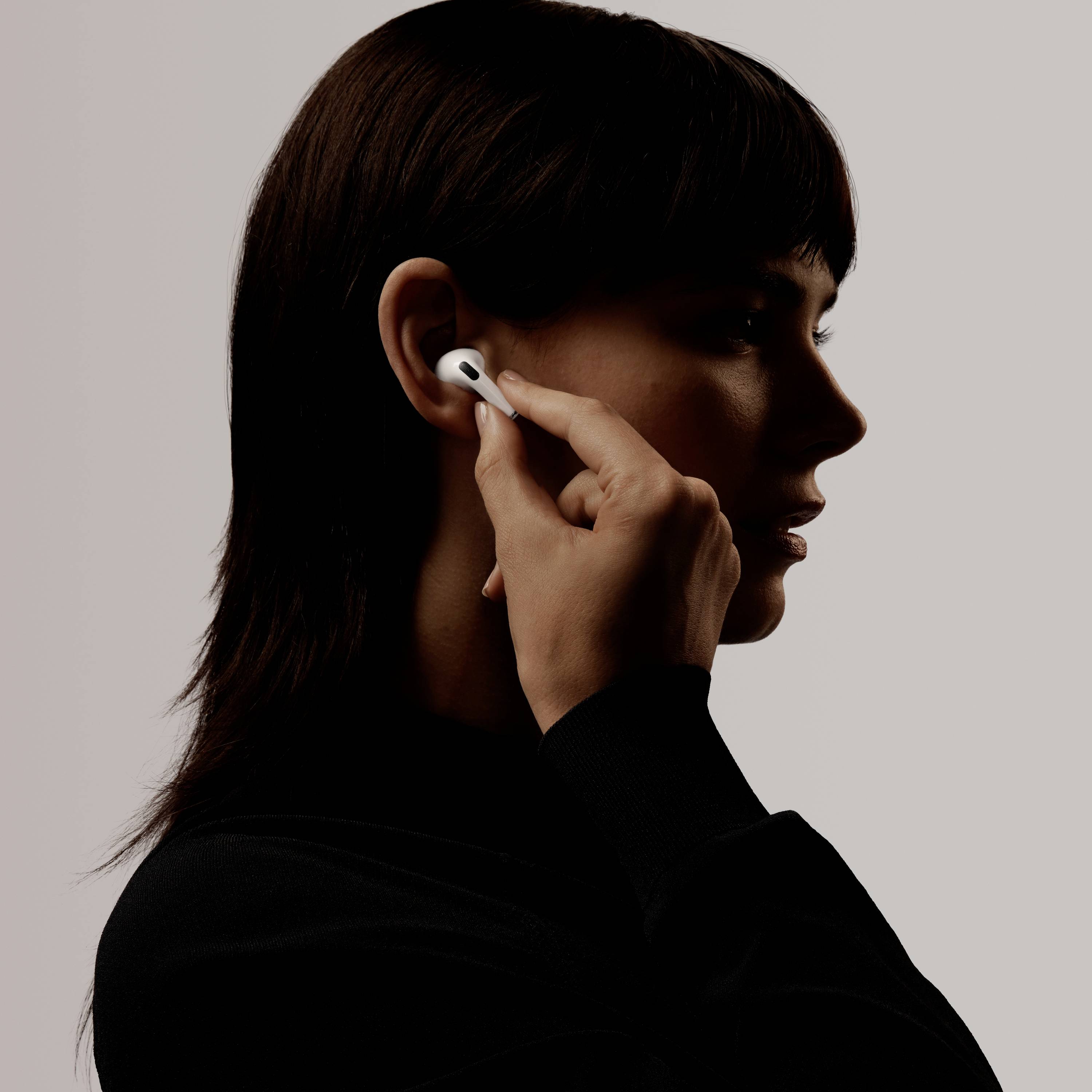 Une personne aux cheveux noirs porte des écouteurs sans fil et en touche un, comme pour contrôler un appel ou la musique.