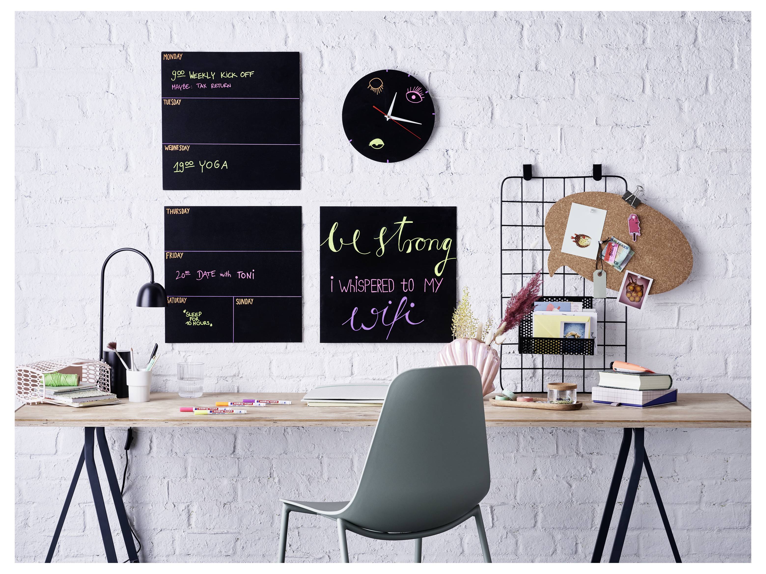 Un bureau à domicile avec une chaise, une lampe, de la papeterie, des livres, une horloge murale et des tableaux d'affichage sur un mur de briques blanches, y compris un tableau de citations avec la devise « Sois forte ».
